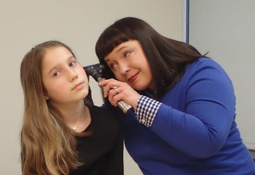 a pediatrician looking in the ear of a young girl
